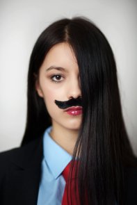 portrait of a young woman dressed up in a man's suit and tie wearing a fake mustache